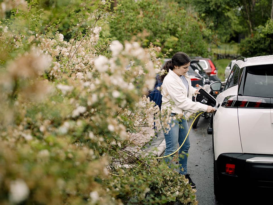 Kvinna står utomhus och kopplar in laddare till elbil, Stockholm
