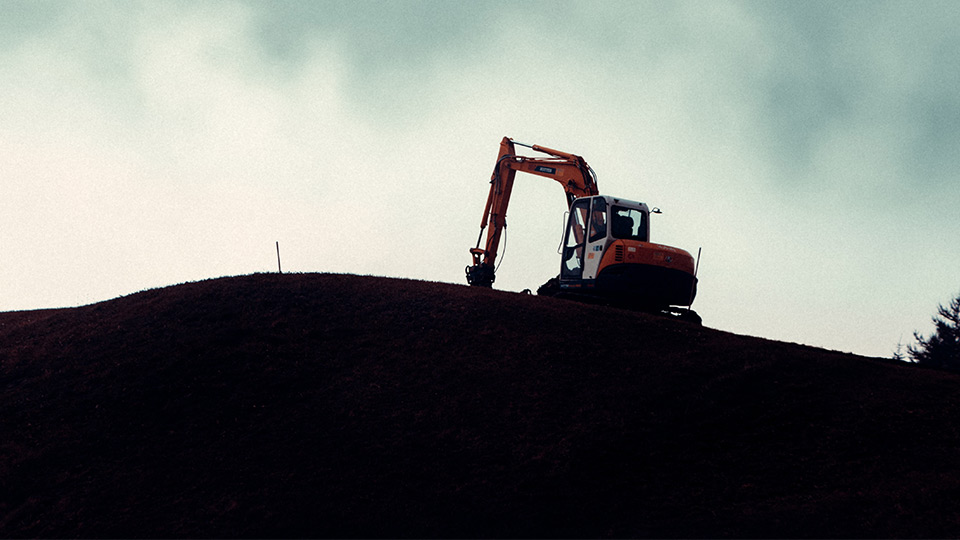 Grävmaskin på kulle i motljus
