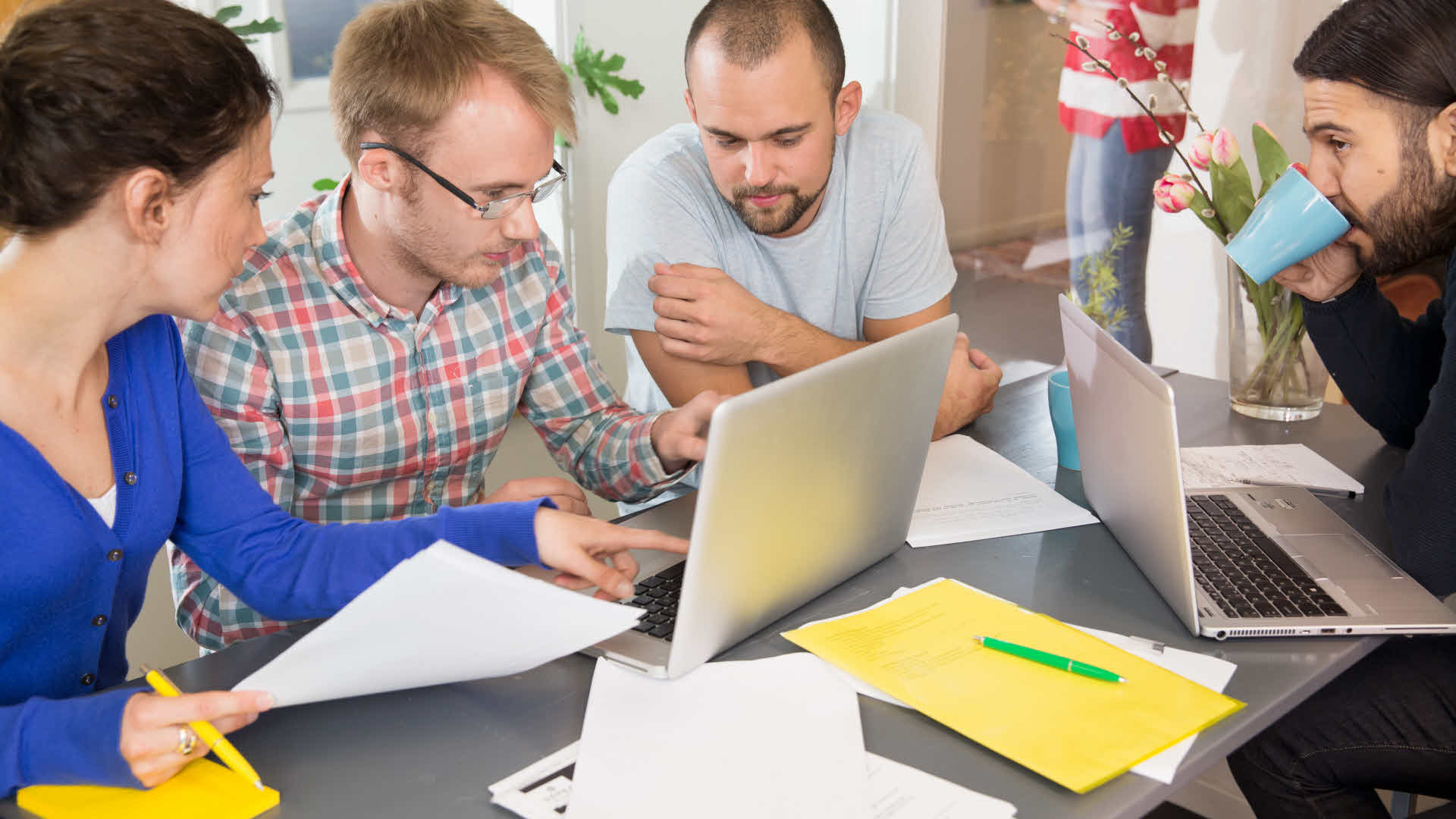 Personer sitter runt ett bord och arbetar med datorer