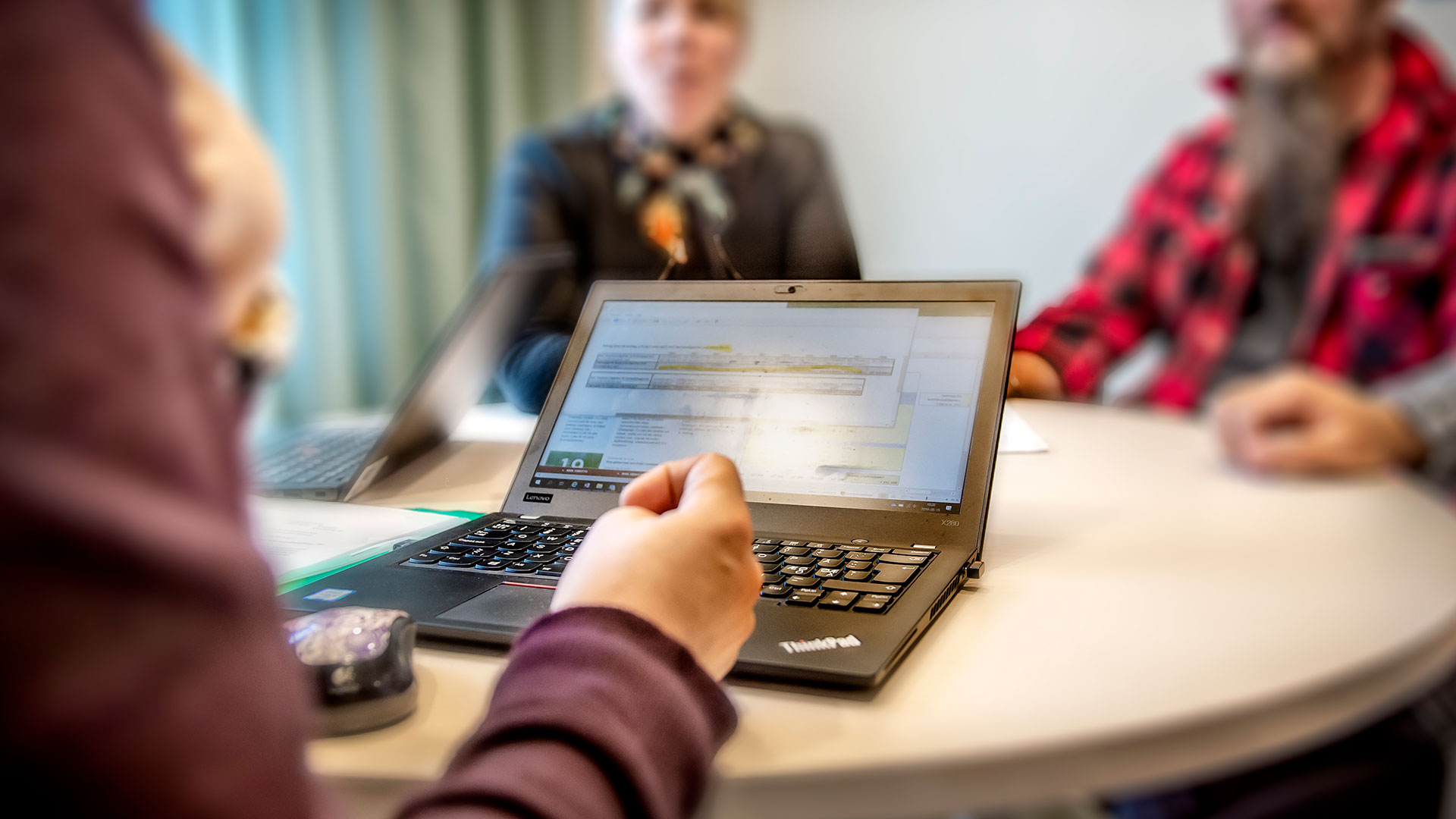 Personer i ett möterum, en person har en bärbar dator uppfälld.