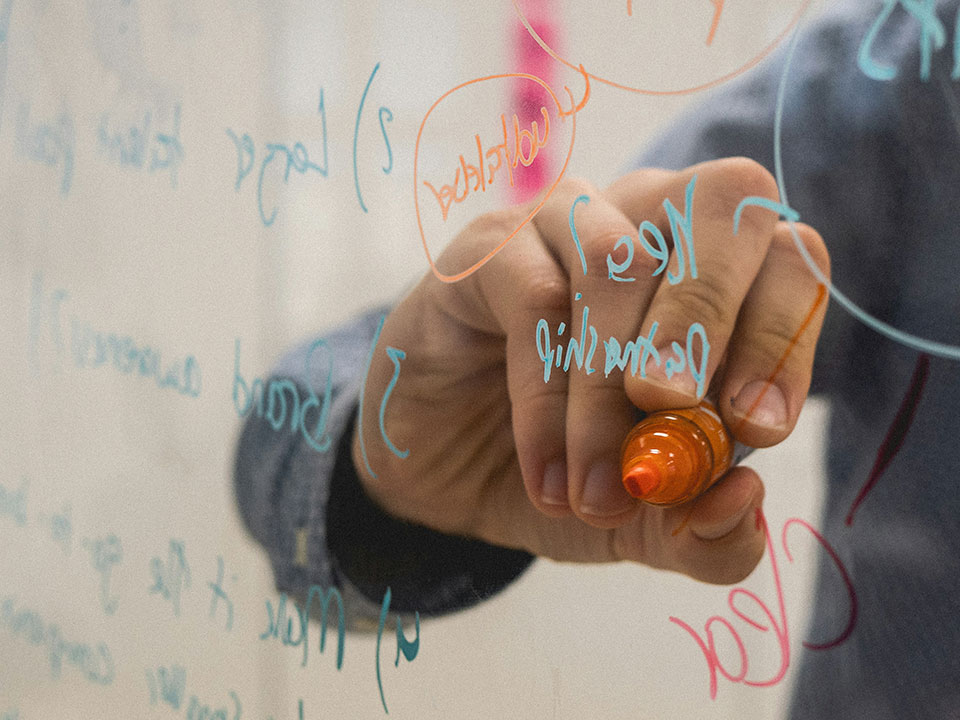 Fotograf: Kvalifik
Bildbyrå: Unsplash En person skriver med en orange penna på en genomskinlig skärm