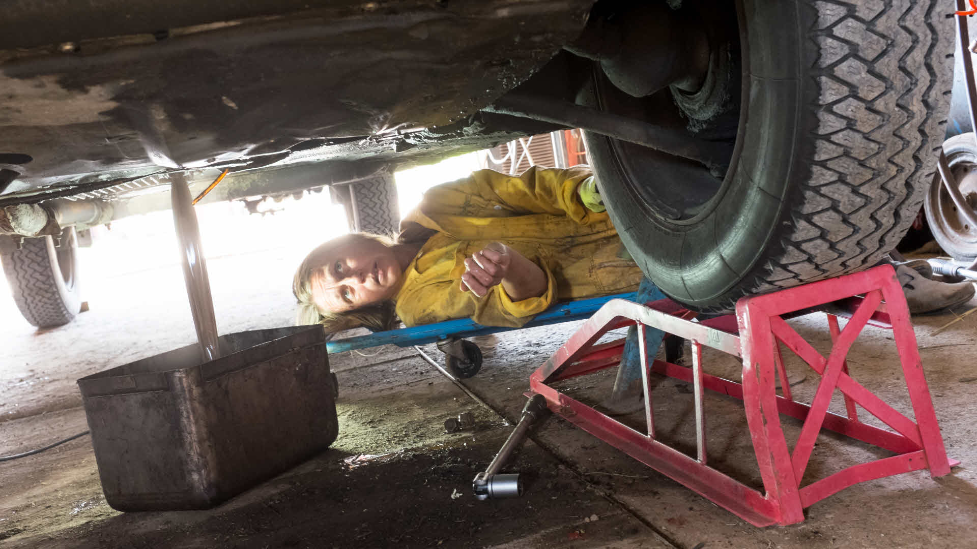 Kvinna ligger under bil och tömmer den på olja