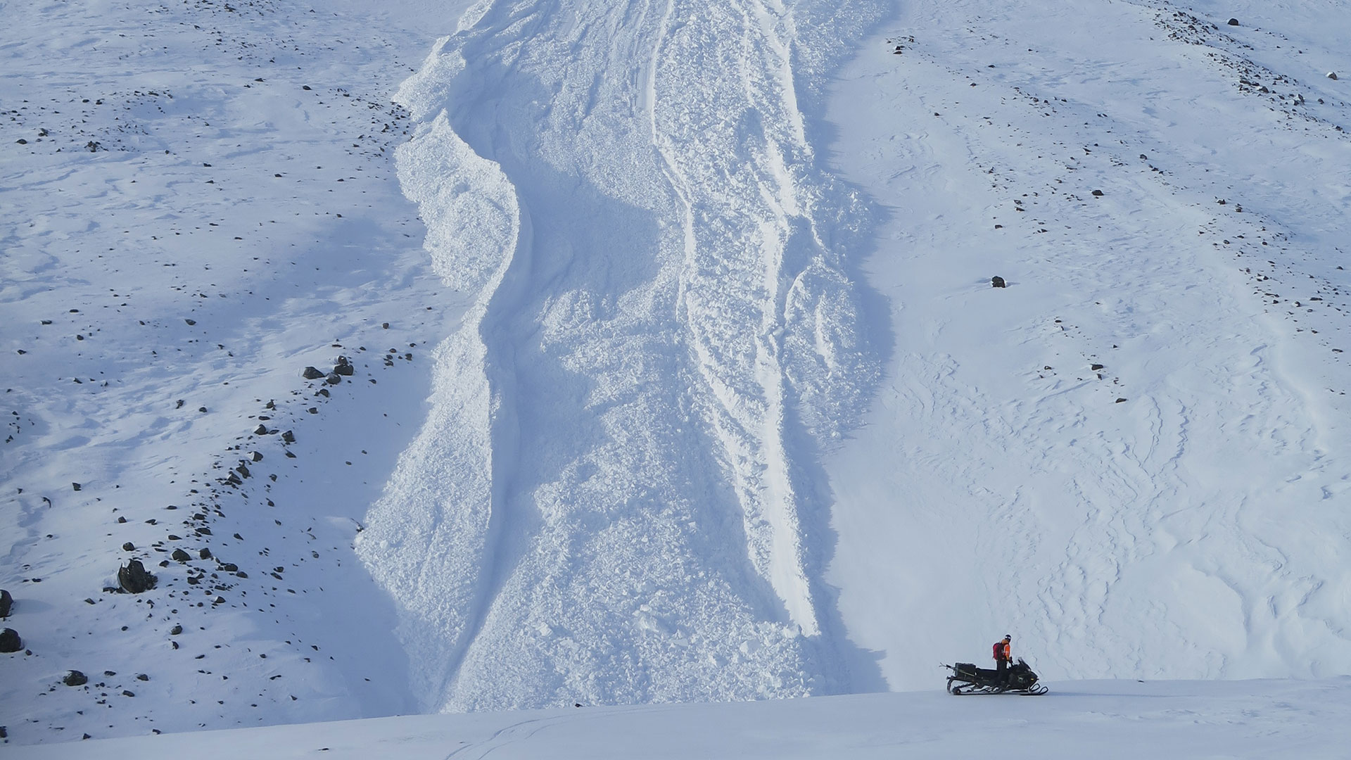 En snöskoter framför ett snötäckt berg.