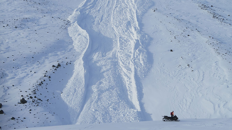 En snöskoter framför ett snötäckt berg.