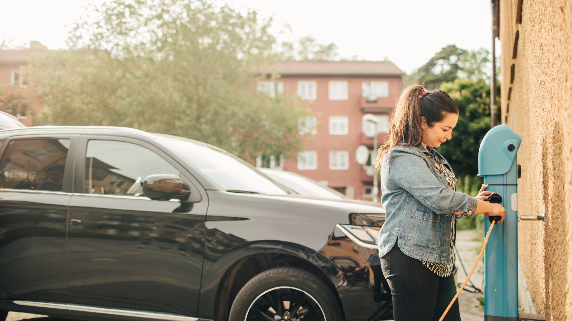 Kvinna ska ladda elbil och ansluter kabel till laddstolpe